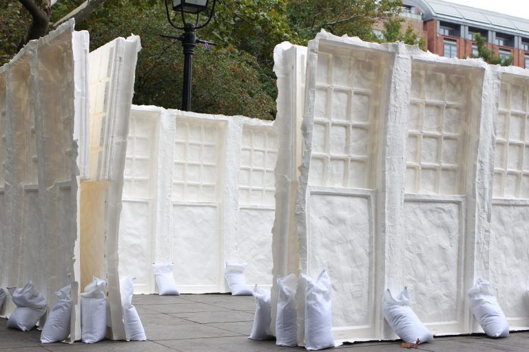 White sculptural relief forms of windows held up by sandbags.