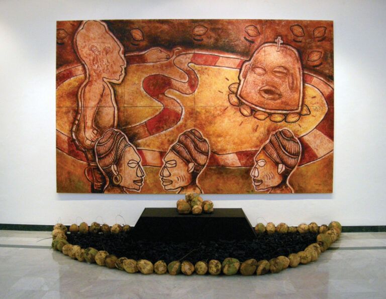 Coconuts are lined around a dark offering table in front of a painting of native people and a snake.