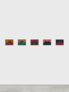 Five framed landscape paintings lined up on a wall. Each one is a mountain painted in an unnatural color with a corresponding unnaturally colored sky.