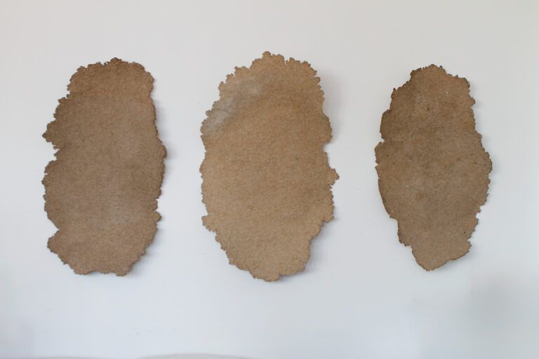 Three brown ellipse-shaped forms are hung on the wall. They are flattened shapes made from recycled material.