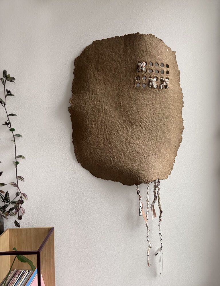 A large cardboard clay form with holes carved into the material to accommodate for braided textiles to be threaded through the openings.