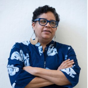 Artist Joey Quiñones stands with their arms crossed, looking to the right.